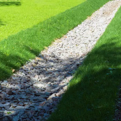 A narrow gravel pathway cuts through a green grassy field, casting a shadow on one side.