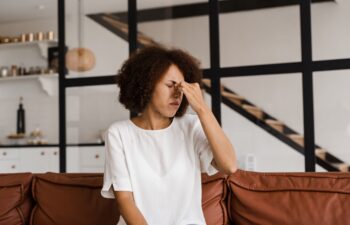 Sick African girl with sinusitis is holding her stuffy nose because she has rhinitis and is planning to go to the ENT doctor